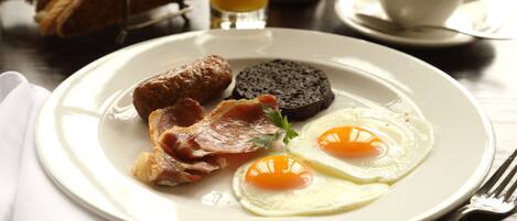 Une assiette de petit-déjeuner avec des œufs, du bacon, des saucisses et de la boudin noir, le tout servi sur une assiette blanche.