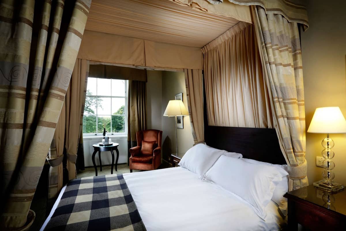 A hotel room with a bed, a chair, a table, a lamp, and a window with curtains.