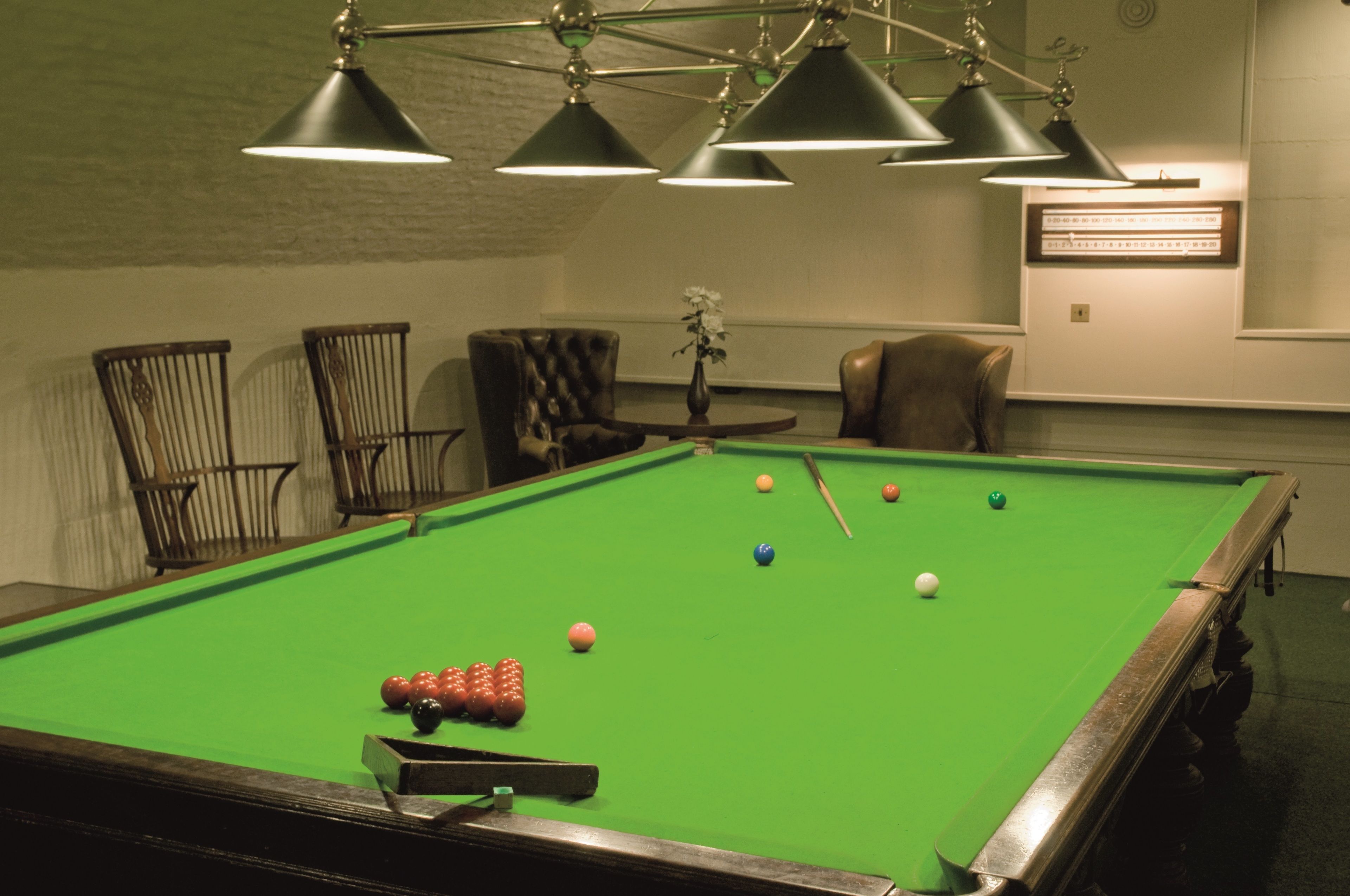 A pool table with balls, chairs, and a clock on the wall.