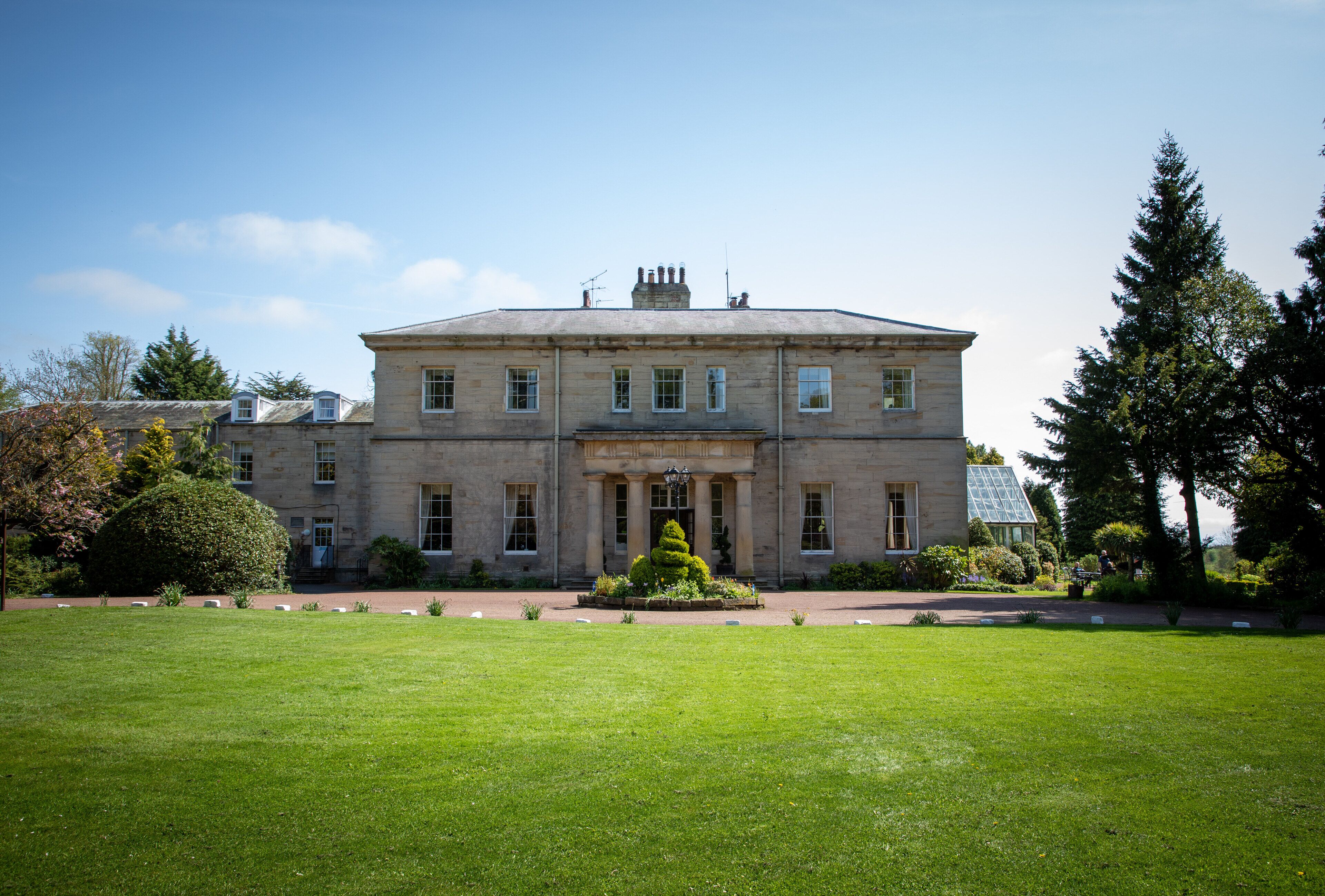 A large, historic building with a symmetrical facade, a central entrance, and a well-maintained lawn in front.