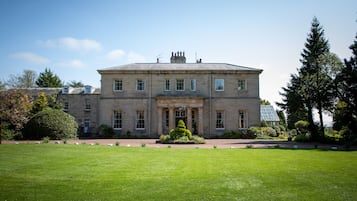 A large, historic building with a symmetrical facade, a central entrance, and a well-maintained lawn in front.