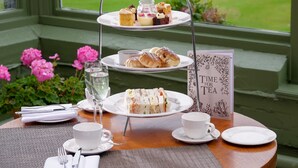 A three-tiered tea service set on a table with a view of a garden through a window. - Macdonald Linden Hall Golf & Country Club (Morpeth)