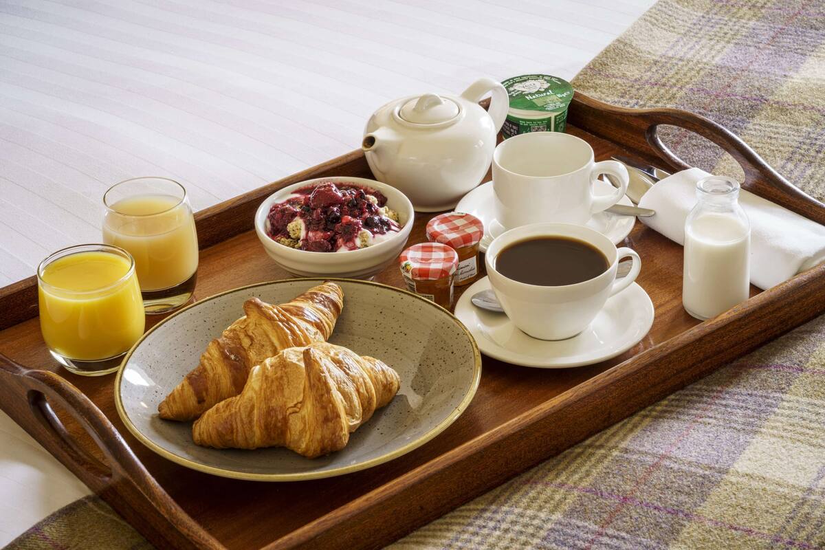 A breakfast tray with croissants, juice, coffee, and a bowl of berries.