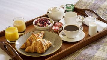 A breakfast tray with croissants, juice, coffee, and a bowl of berries.
