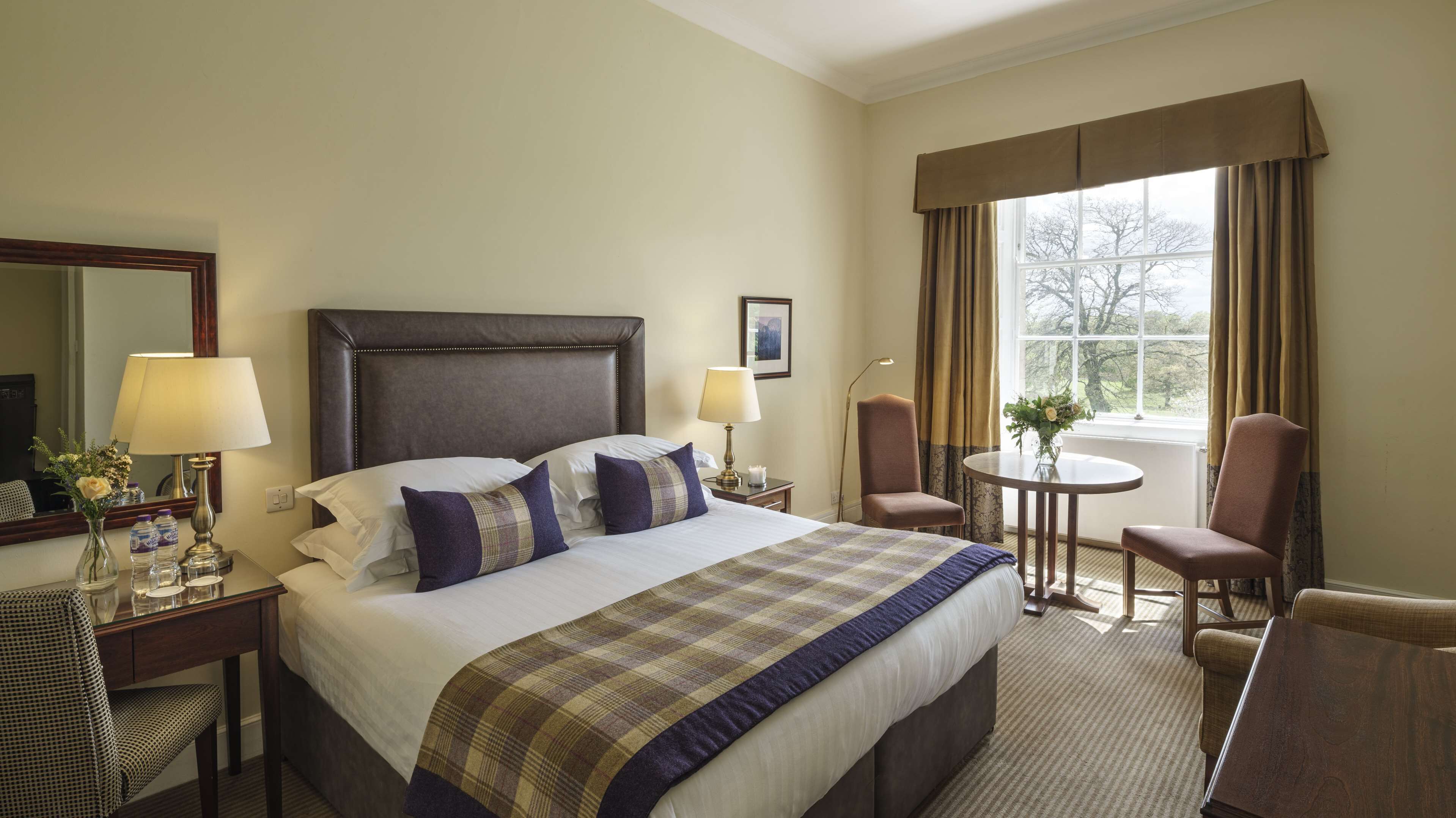 A hotel room with a large bed, two bedside lamps, a chair, a small table, and a window with curtains.
