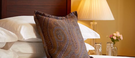 A neatly made bed with a patterned pillow, a bedside lamp, and a vase with flowers.