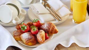 A breakfast setting with pastries, strawberries, a cup of coffee, a teapot, and a glass of orange juice.