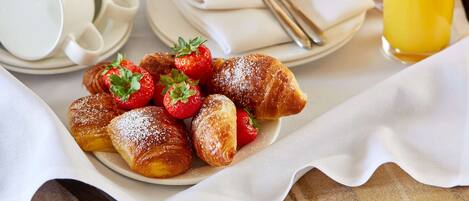 A breakfast setting with pastries, strawberries, a cup of coffee, a teapot, and a glass of orange juice.