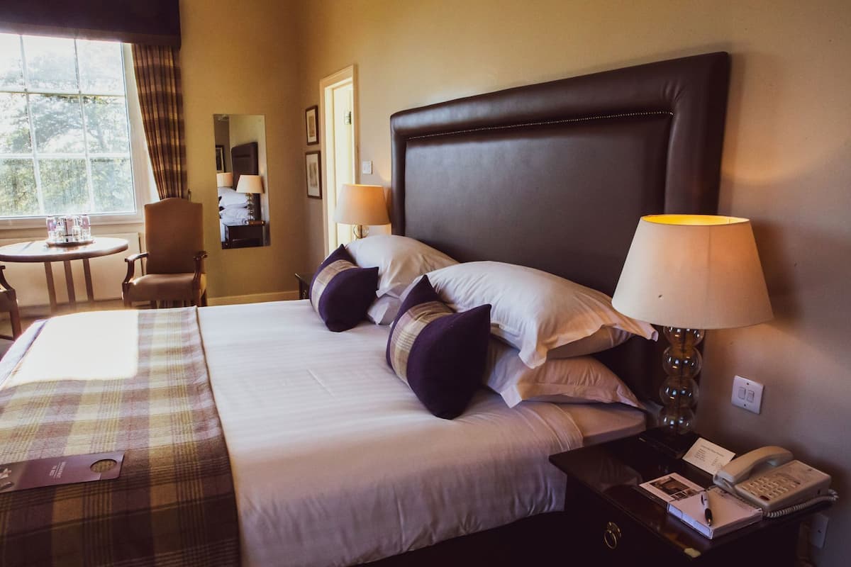 A hotel room with a large bed, two bedside lamps, a desk with a phone, and a chair.