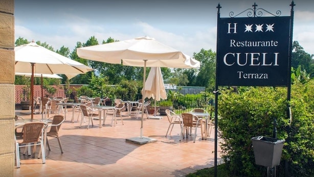 An outdoor patio with tables and chairs, a sign for Restaurante CUELI, and a trash bin. - Hotel Cueli (Santillana del Mar)