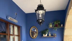 A room with a blue wall, wicker furniture, a white sofa, a potted plant, a hanging lantern, and a mirror. - Hotel Cueli (Santillana del Mar)