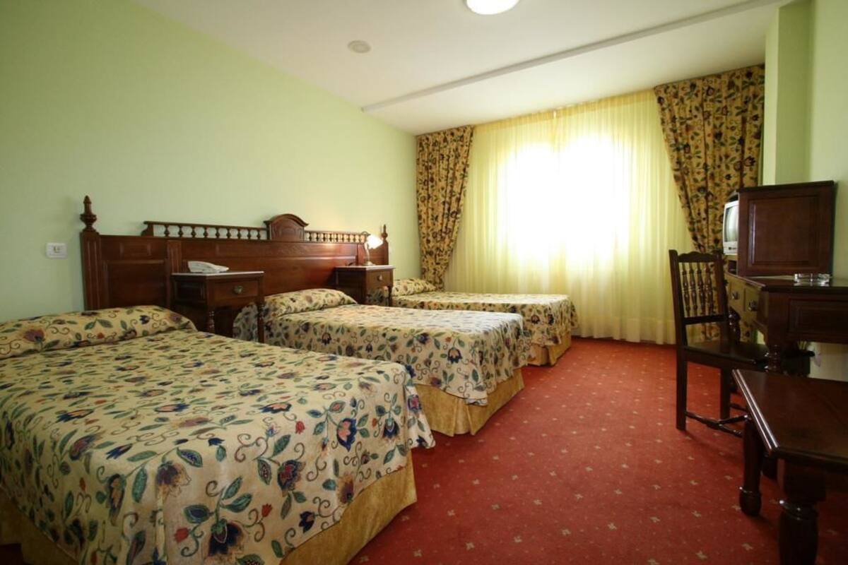 Een hotelkamer met drie eenpersoonsbedden, een houten hoofdbord, een televisie en een bureau met een stoel.