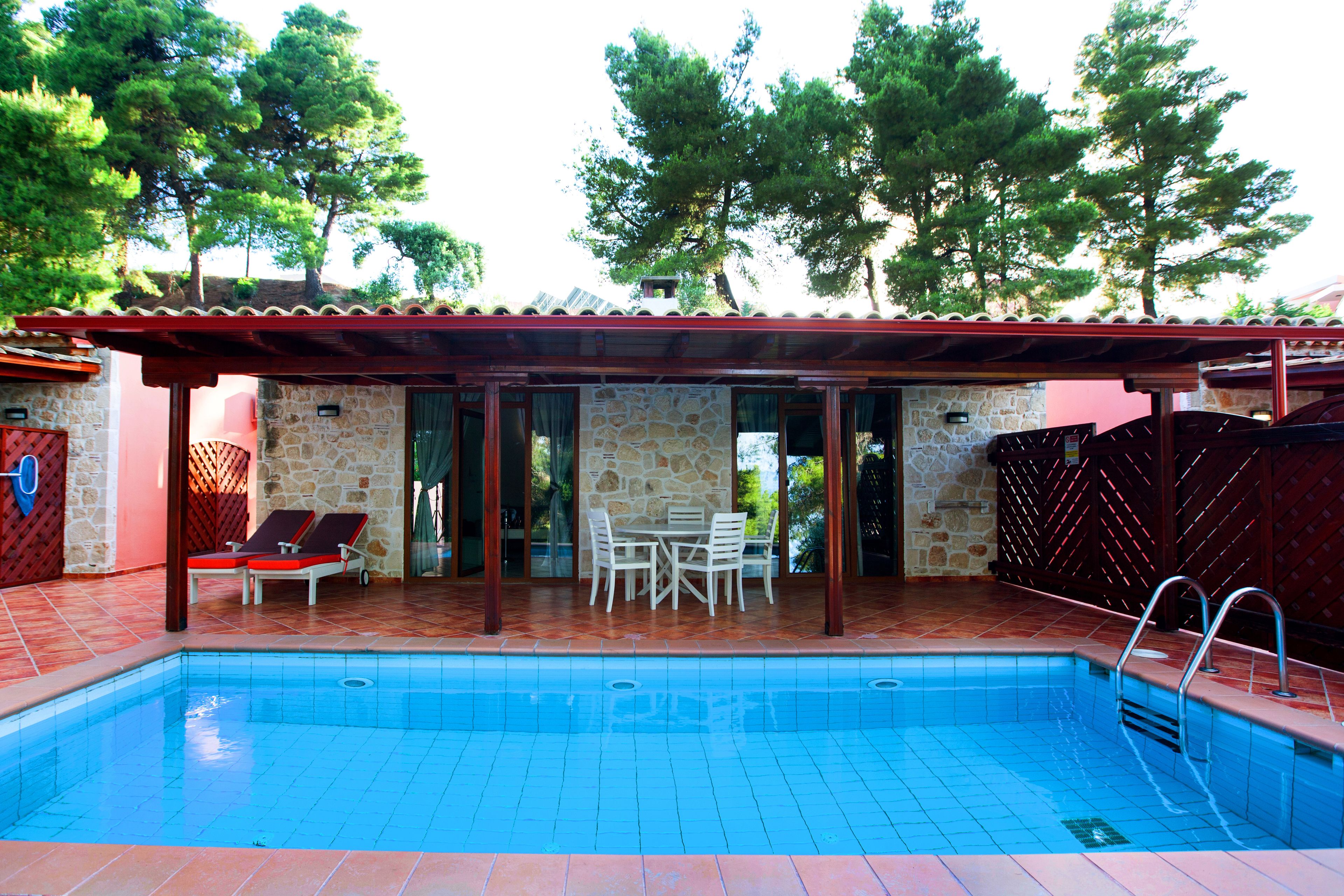 A swimming pool with a stone wall and a covered patio area with a table and chairs.