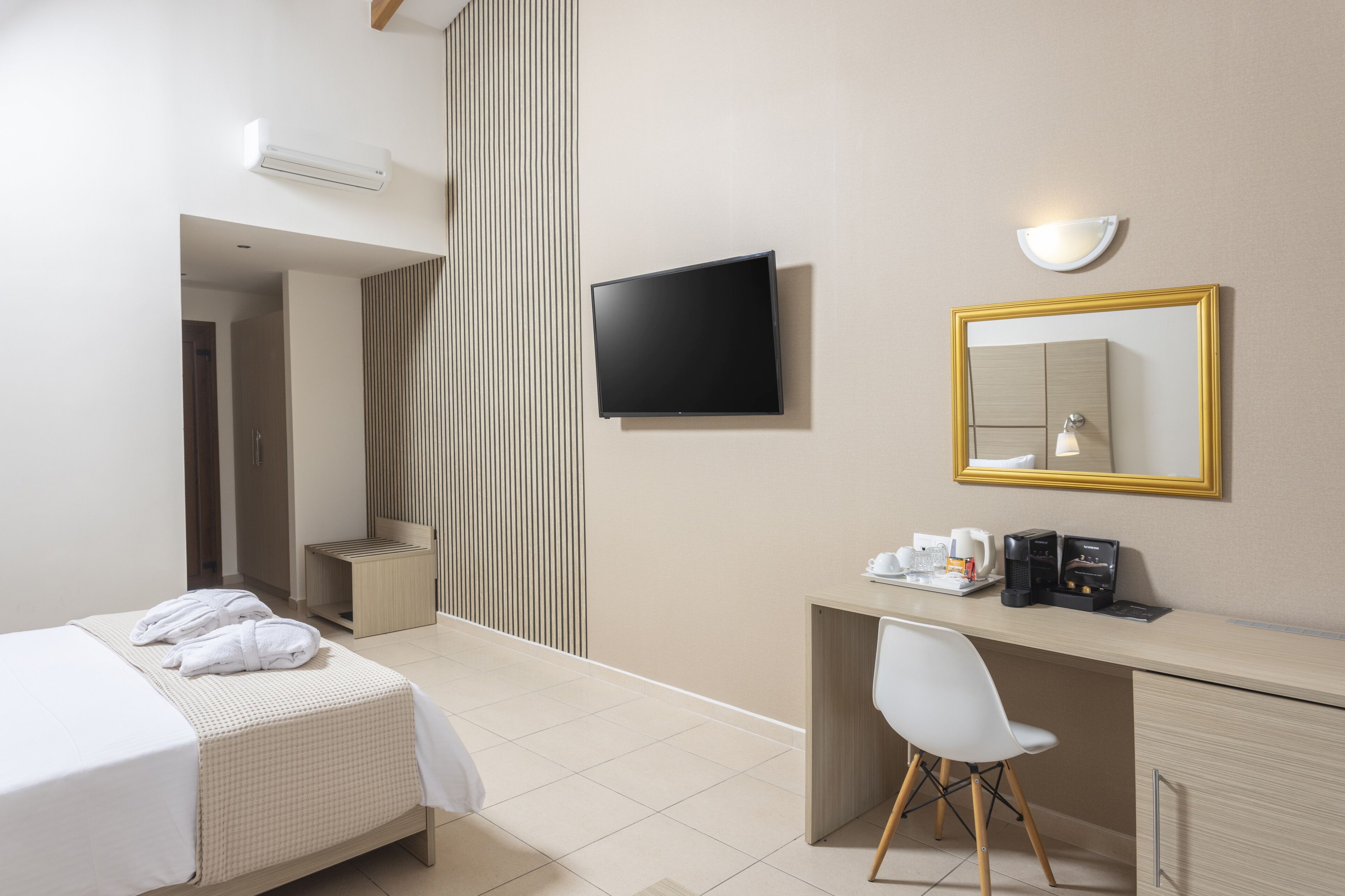 Habitación de hotel con cama, escritorio con silla, televisor, espejo y cafetera.