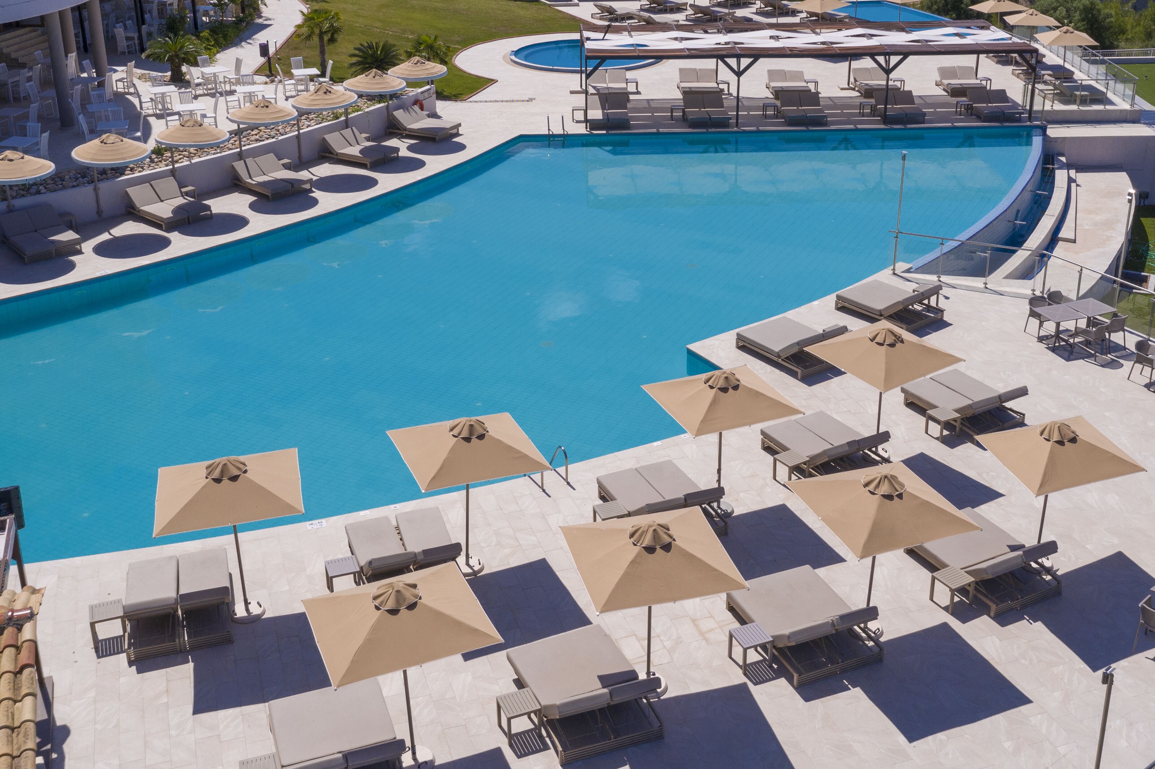 Ein großer Pool mit Liegestühlen und Sonnenschirmen, umgeben von einer Terrasse mit Stühlen und Tischen.