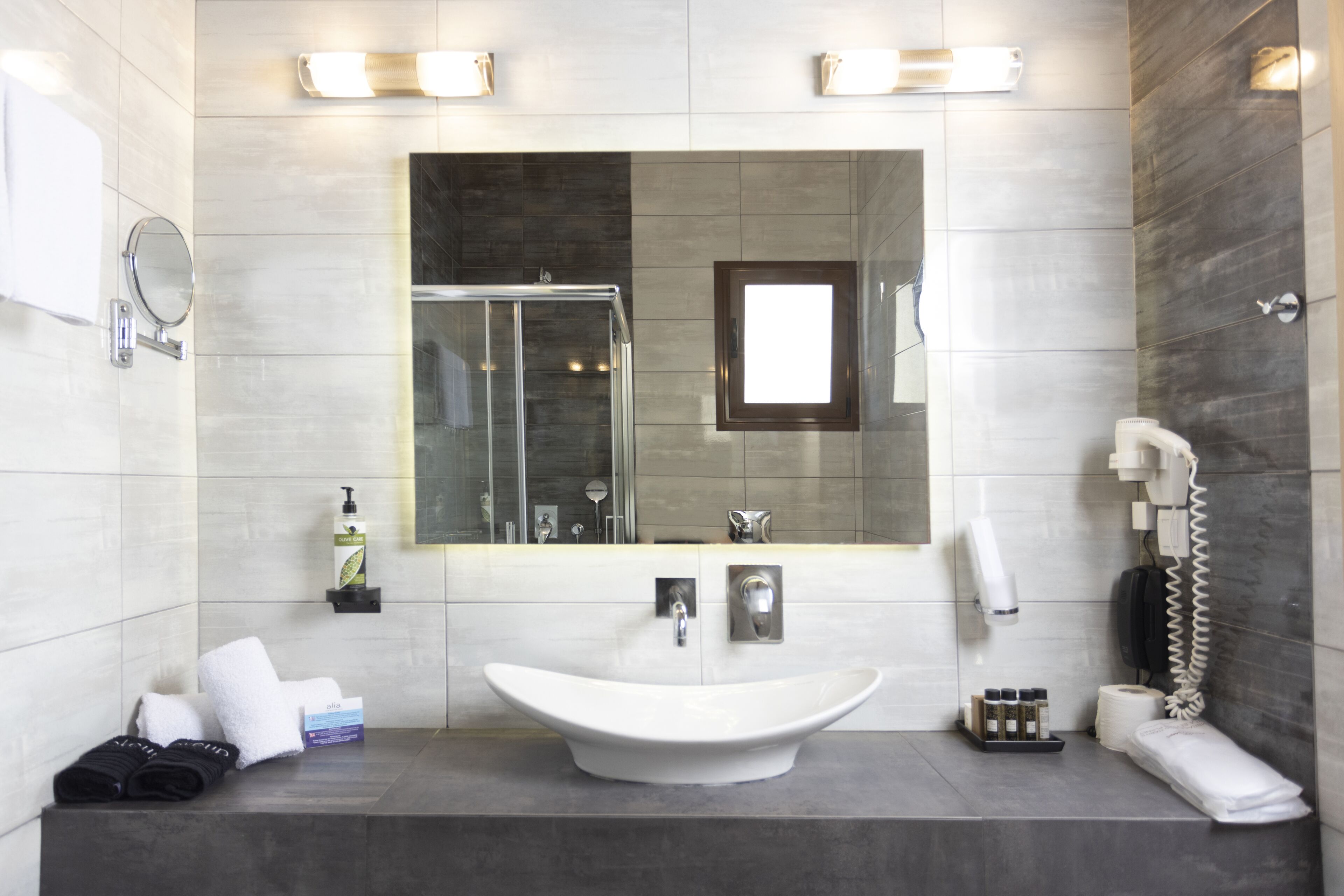 A modern bathroom with a large mirror, a vessel sink, a glass shower enclosure, and a telephone.