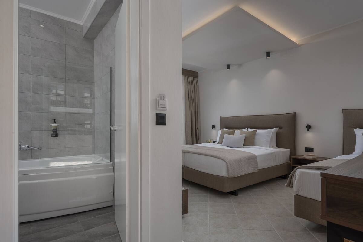 Une chambre d’hôtel moderne dotée d’une grande baignoire, d’un lit double avec une tête de lit et d’une table de chevet.