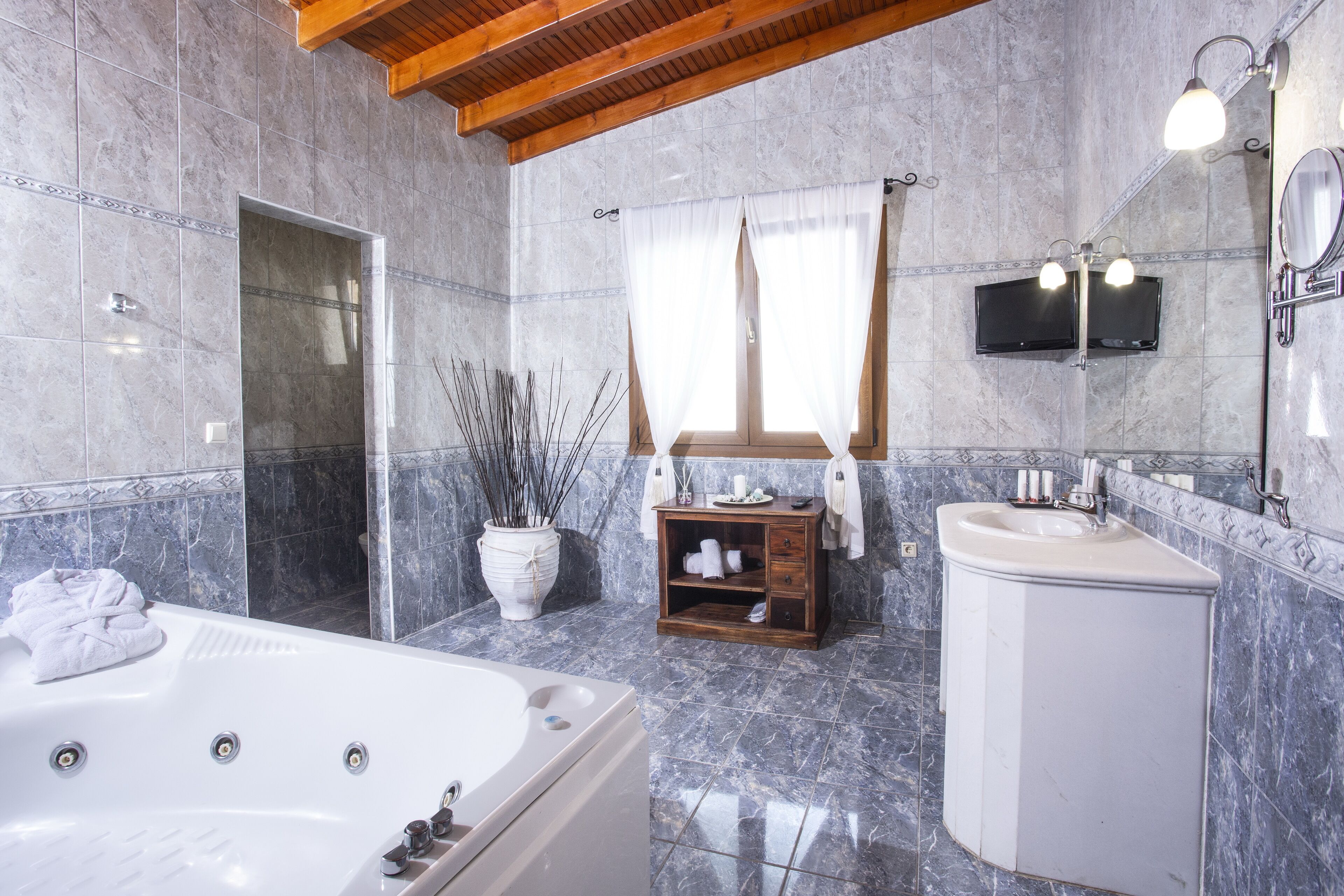 Un baño con una bañera grande, un tocador de madera, un espejo y un televisor montado en la pared.