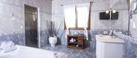 Un baño con una bañera grande, un tocador de madera, un espejo y un televisor montado en la pared.