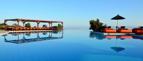 A clear blue pool with lounge chairs and umbrellas, reflecting the sky and surroundings.