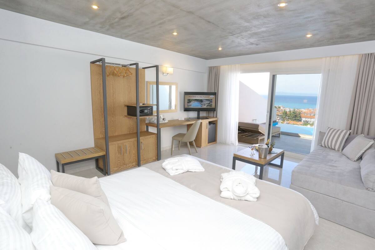 Une chambre d’hôtel moderne équipée d’un lit, d’un bureau, d’une télévision et d’un balcon avec vue sur la mer.
