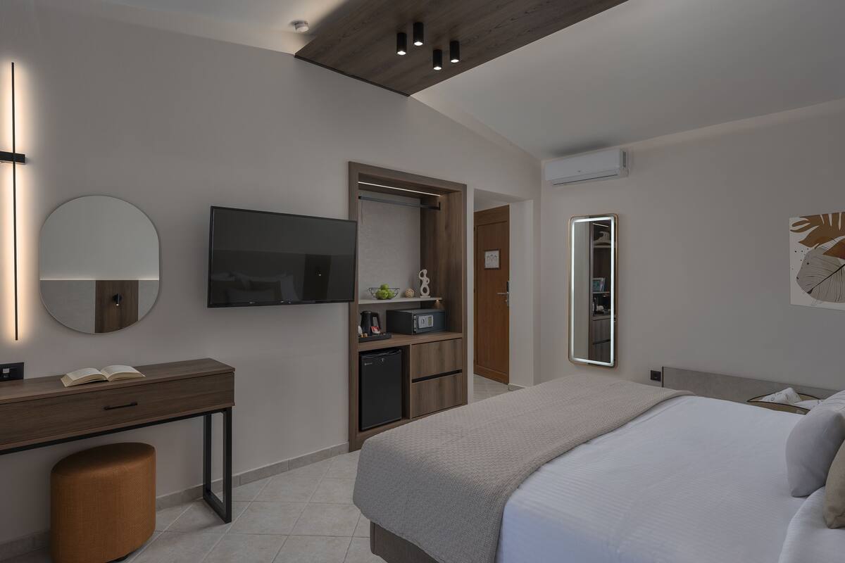 Une chambre d’hôtel moderne équipée d’un lit, d’un bureau, d’un miroir, d’une télévision et d’une kitchenette.
