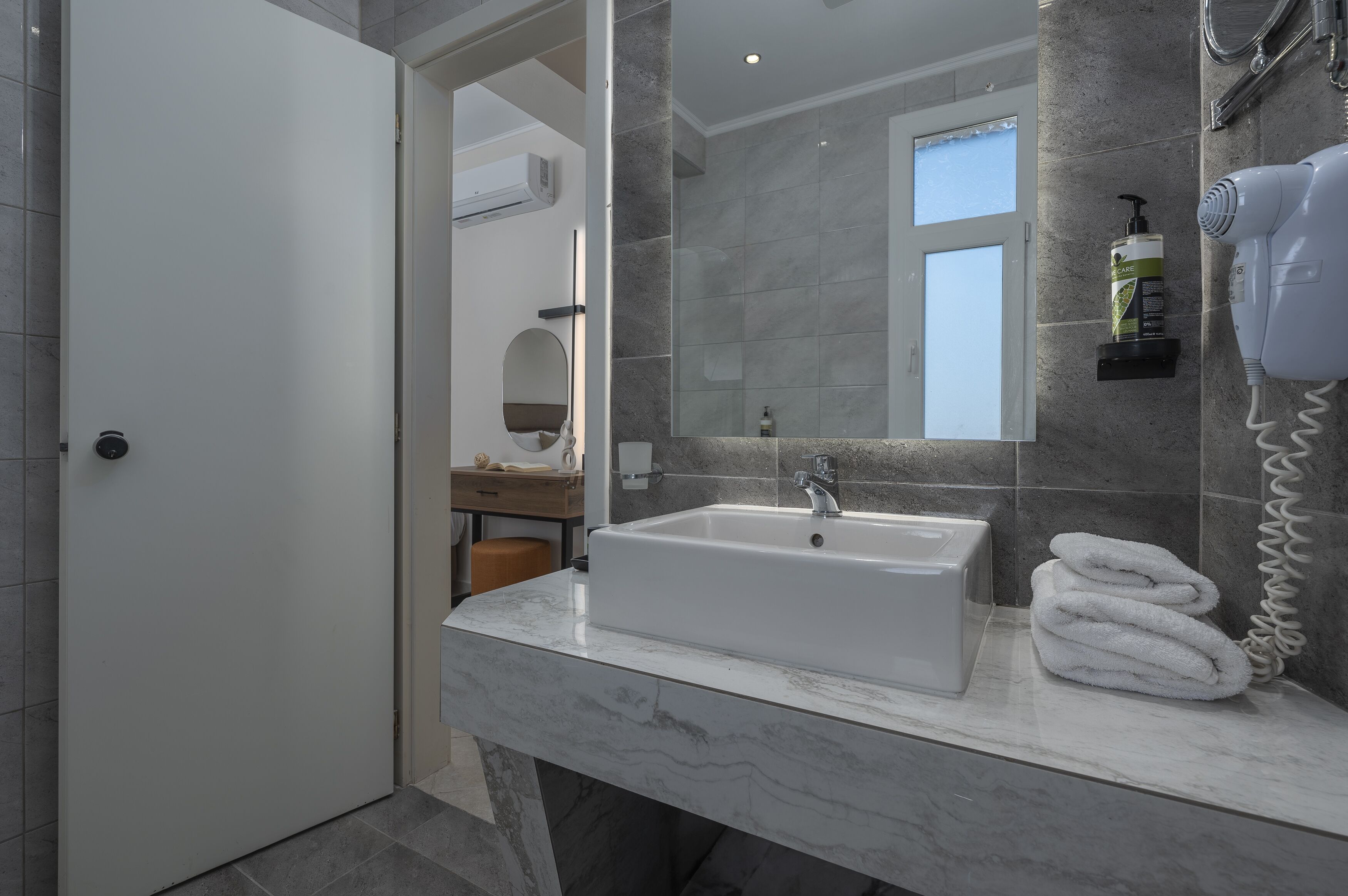 A modern bathroom with a white sink, a towel rack, a mirror, and a hairdryer on the counter.
