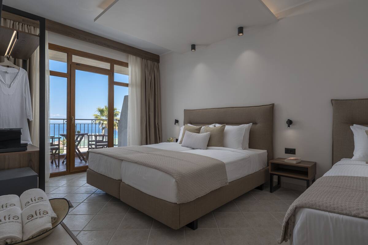 Une chambre d’hôtel avec un grand lit, une table de chevet, une armoire et un balcon donnant sur la mer.