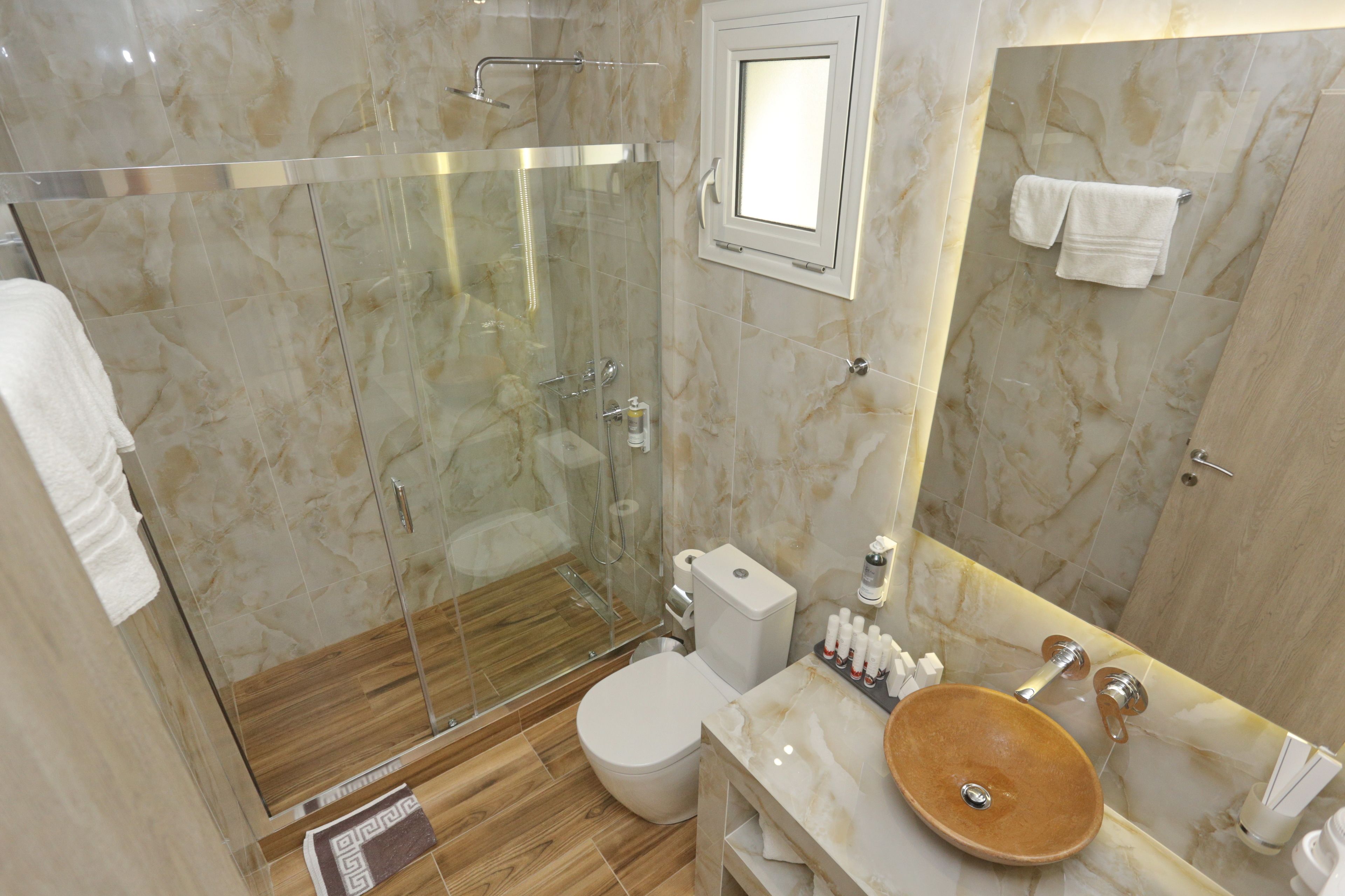 Une salle de bain moderne dotée d’une douche à parois de verre, d’un sol carrelé en marbre, d’un meuble-lavabo en bois avec un vasque et de toilettes.