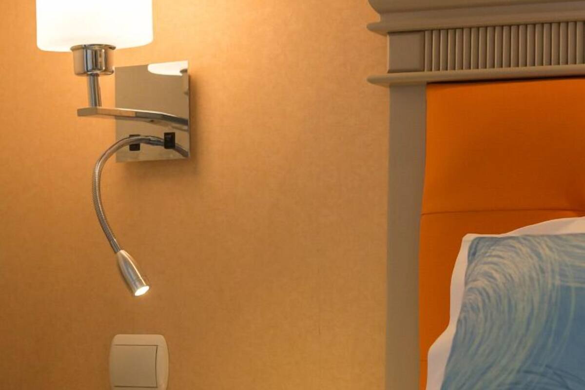 A hotel room with a bed, a nightstand, a lamp, and a wall-mounted light fixture.