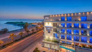 Un hotel de varios pisos con piscina, situado cerca de la costa con vistas al mar y una isla distante.