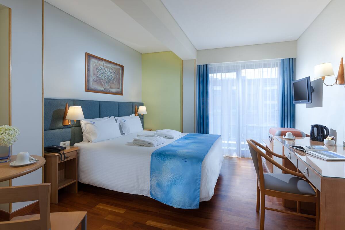 A hotel room with a bed, desk, chair, and a TV.