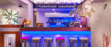 A bar area with a blue-lit counter, multiple stools, and a variety of bottles and glasses.
