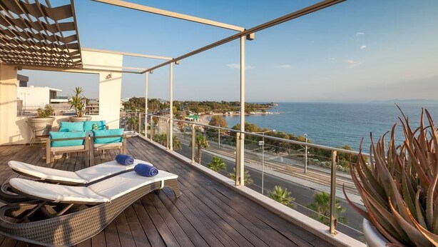 Un balcón con vistas al mar, una silla de lounge, una mesita y una planta en maceta.