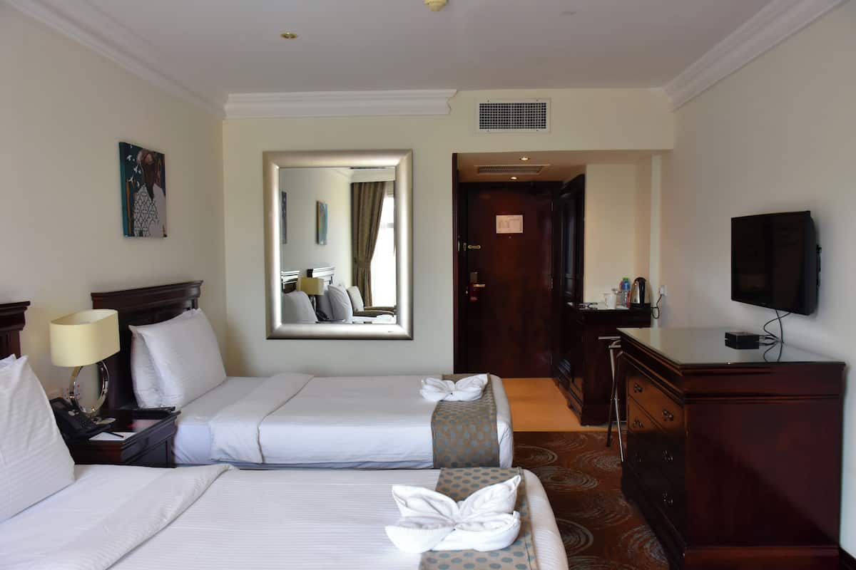 Quarto de hotel com duas camas, televisão, escrivaninha e espelho.