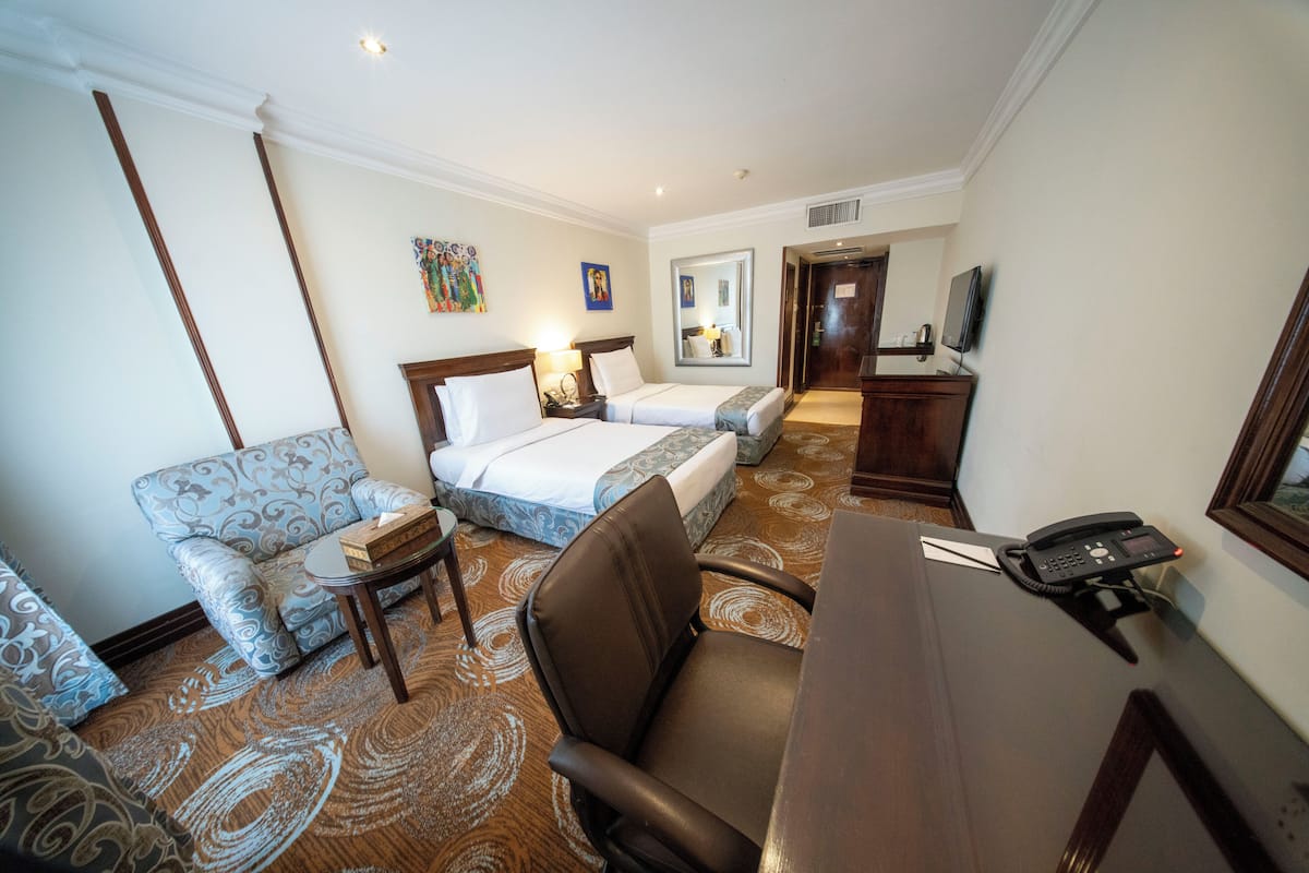 Quarto de hotel com cama, sofá, escrivaninha com telefone e televisão.