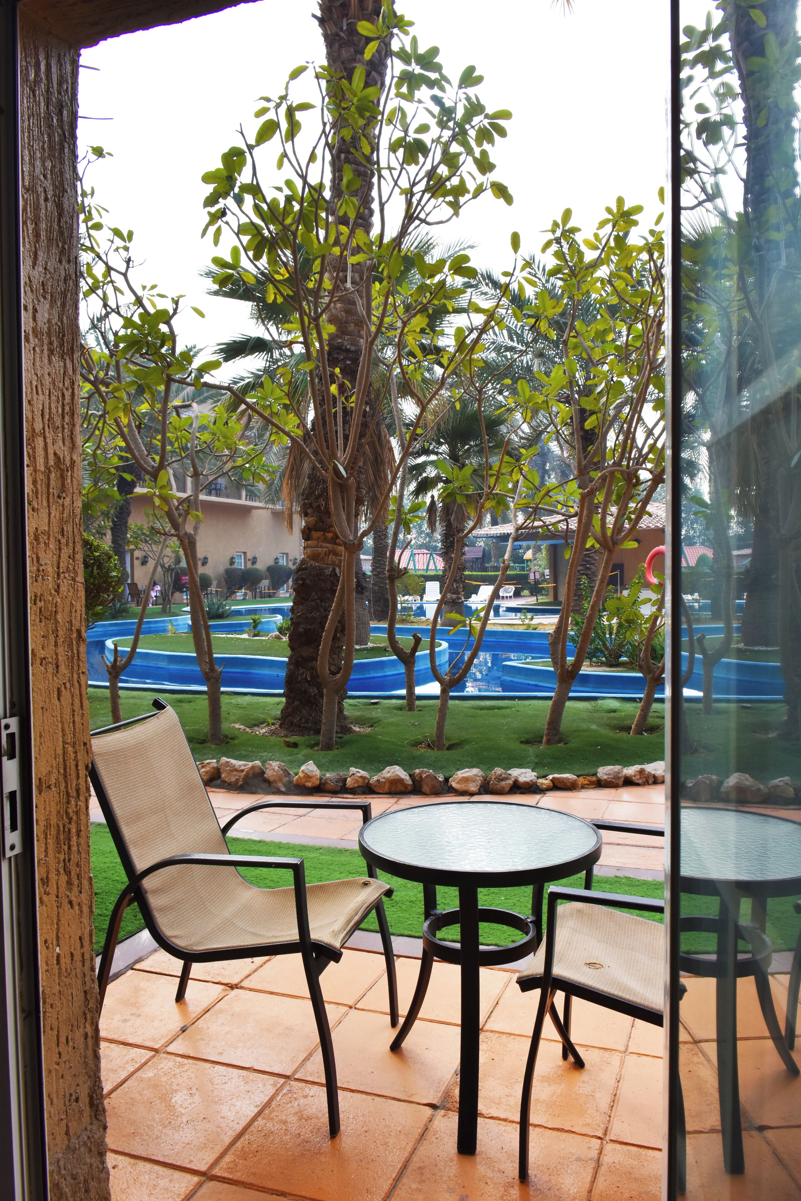 Un patio con due tavoli e sedie, una palma e vista su una piscina.