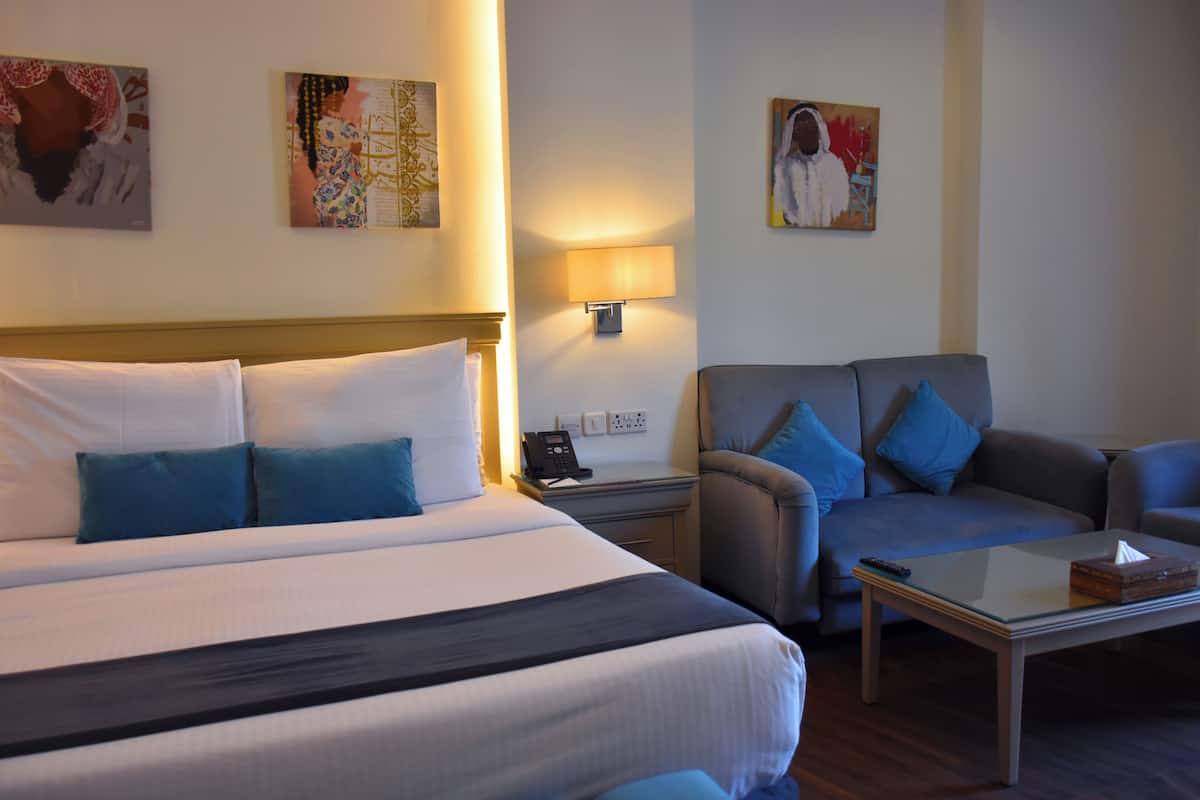 Quarto de hotel com uma cama grande, um sofá, uma mesa de centro e uma mesa de cabeceira com abajur.