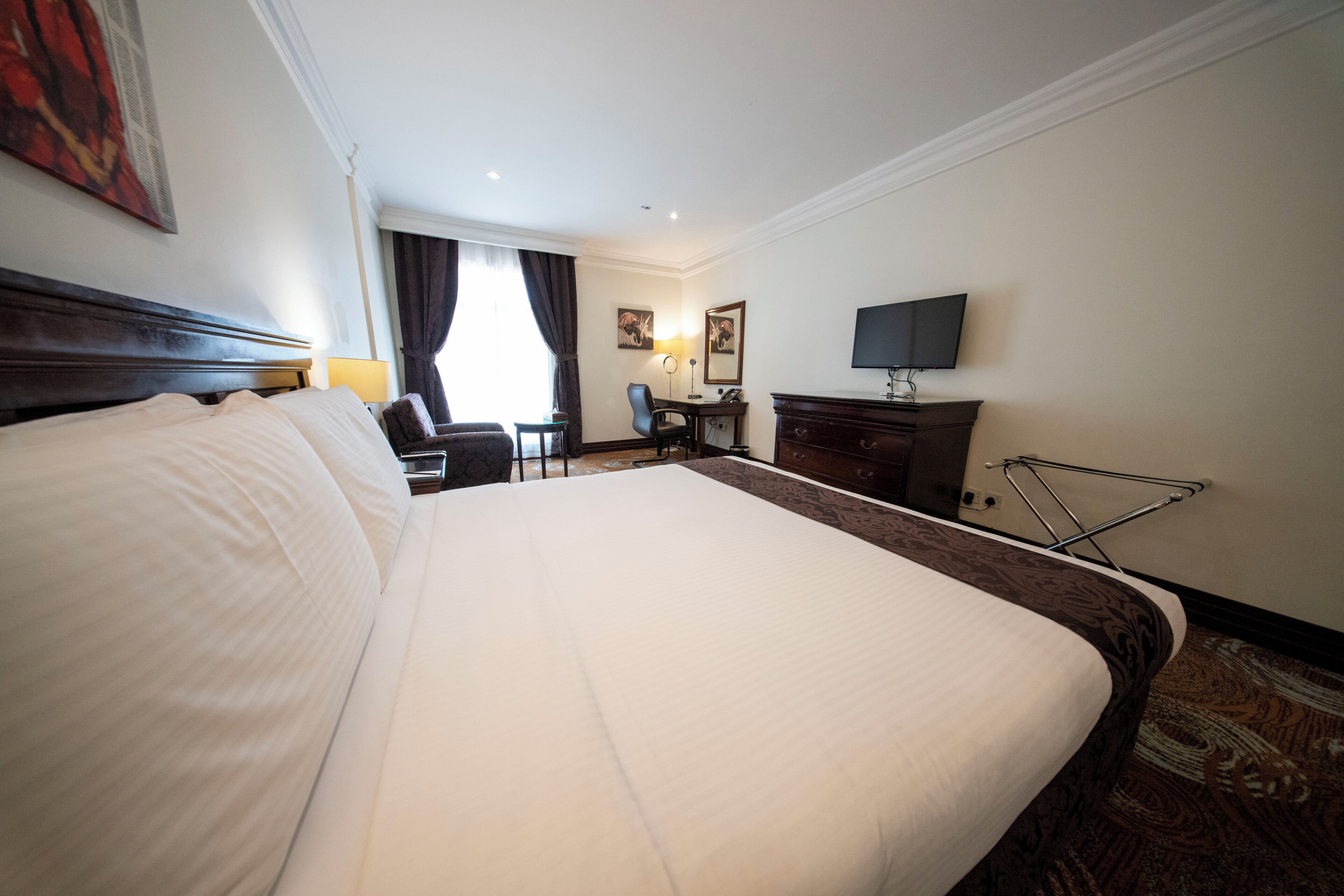 A hotel room with a large bed, a desk, a chair, a television, and a window with curtains.