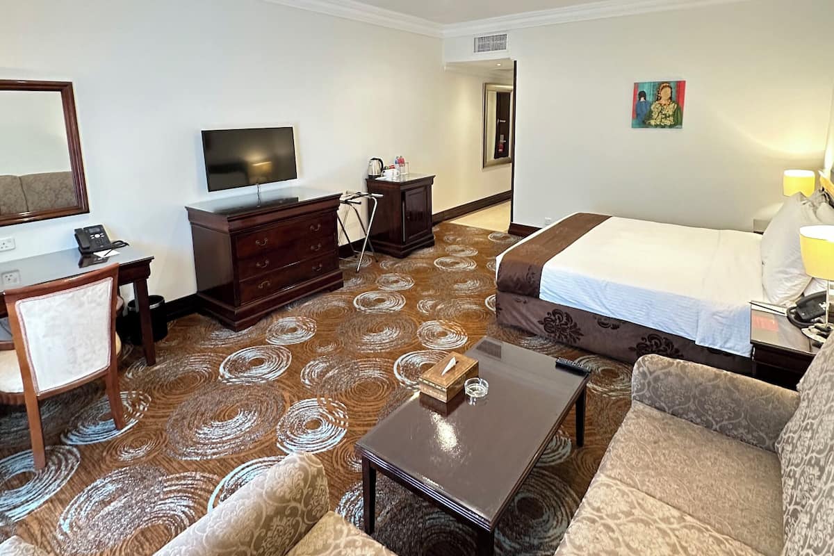 Quarto de hotel com cama, sofá, televisão, cômoda e tapete estampado.