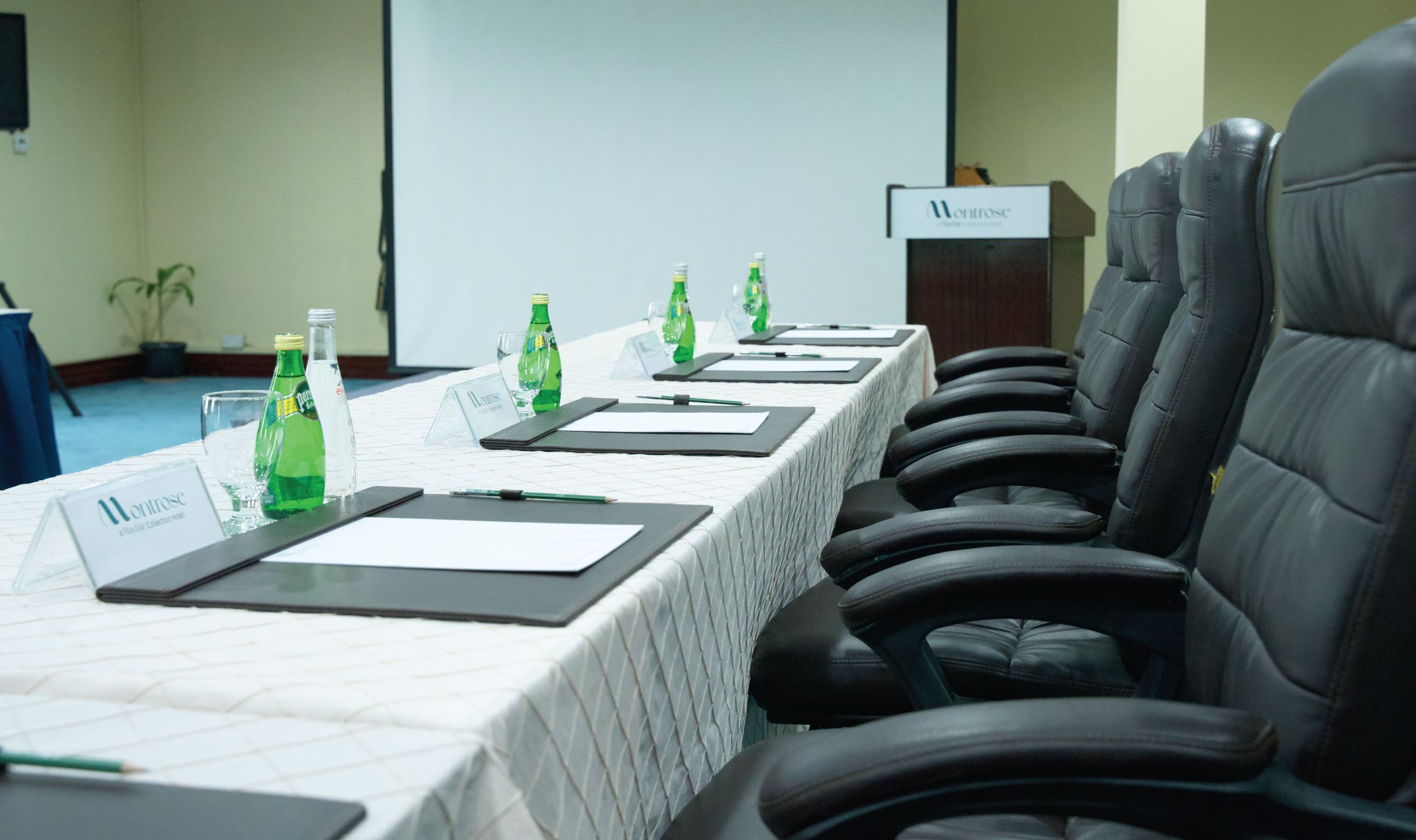 Un salón de conferencias con una larga mesa, tarjetas de identificación, botellas de agua y sillas de cuero negro.