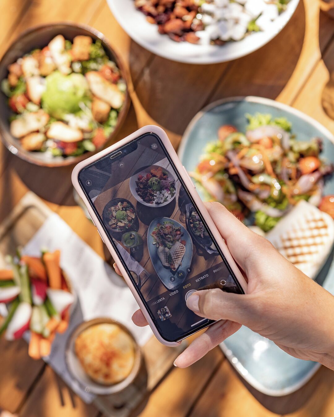 A person holding a smartphone displaying a photo of various dishes.