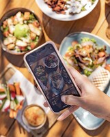 A person holding a smartphone displaying a photo of various dishes.
