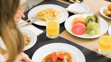 Une table dressée pour le petit-déjeuner, avec des assiettes remplies de nourriture, un verre de jus d’orange et un sapin de Noël en arrière-plan.