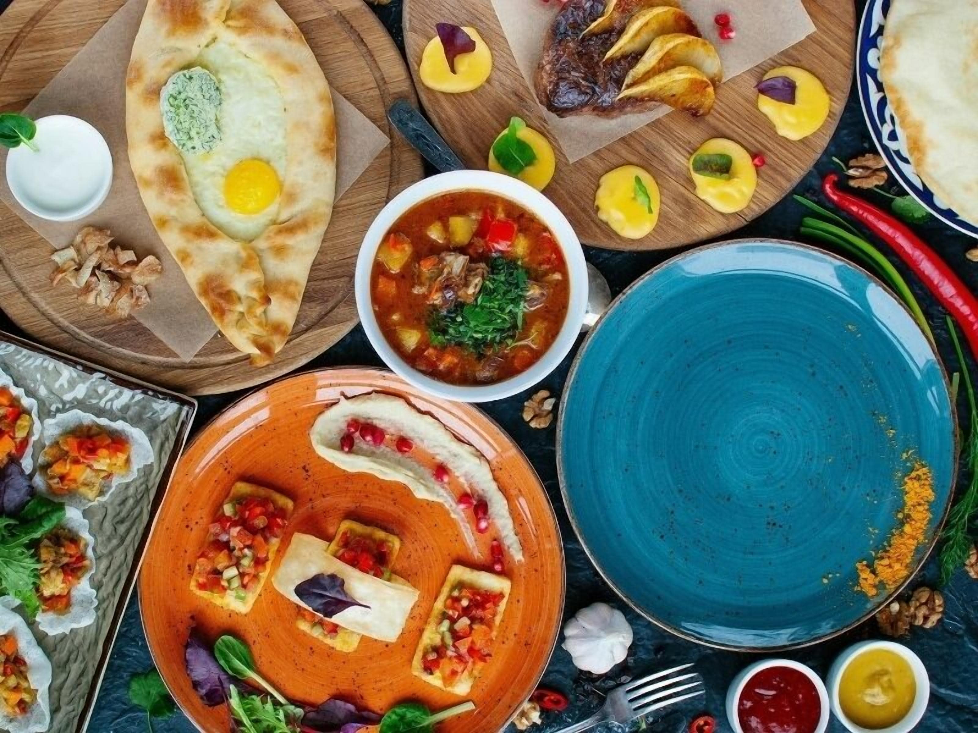Diversos pratos, incluindo pães achatados, uma tigela de sopa e um prato com molho vermelho e legumes.