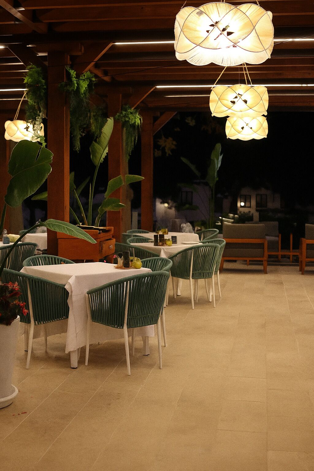 An outdoor dining area with tables and chairs, hanging lamps, and potted plants.