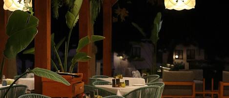 An outdoor dining area with tables and chairs, hanging lamps, and potted plants.