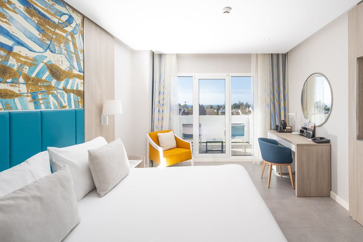 Ein Hotelzimmer mit einem großen Bett, einem Schreibtisch mit Stuhl, einem Fernseher und einem Balkon mit Blick.