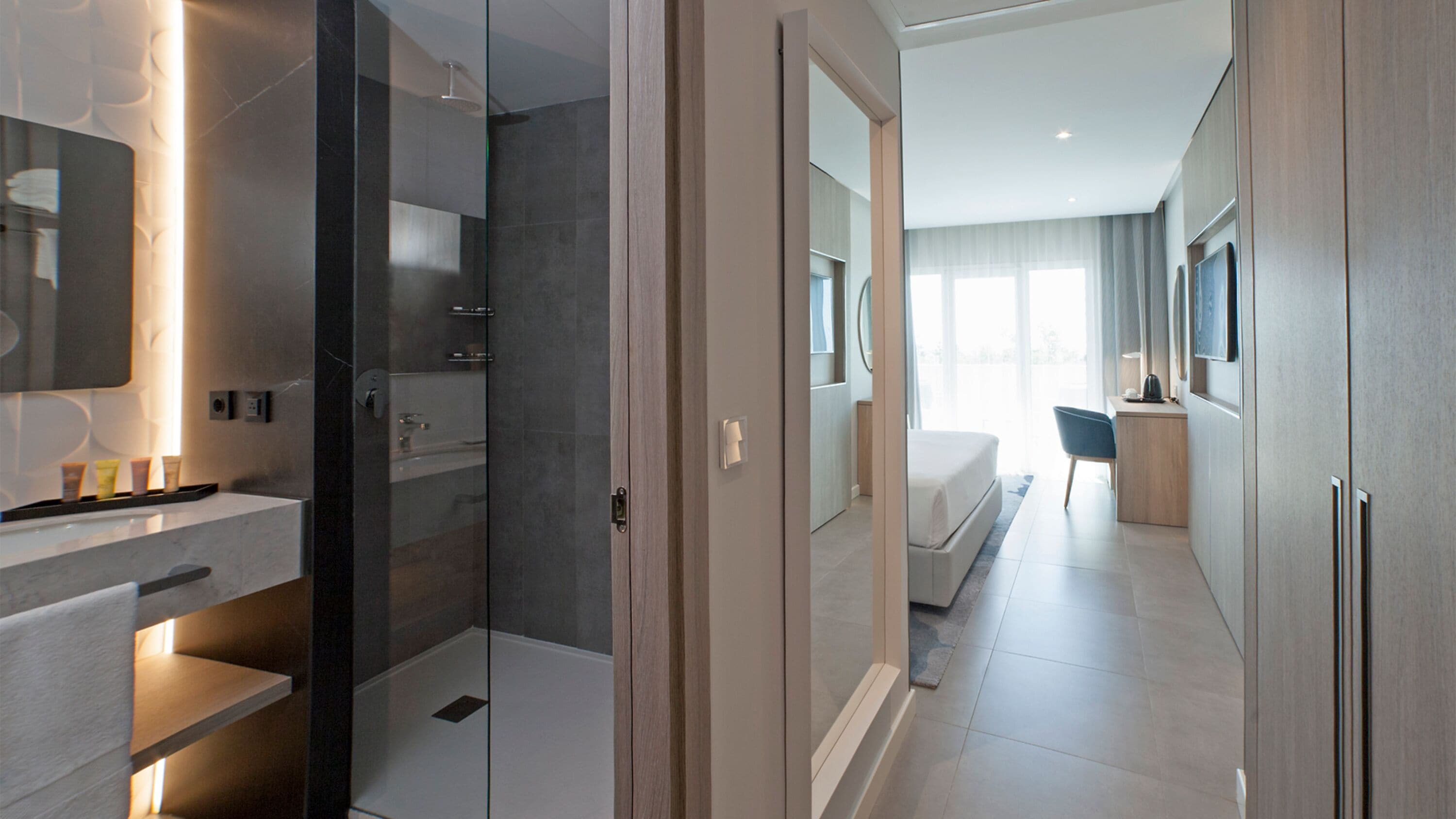 Une chambre d’hôtel moderne dotée d’une douche à parois de verre, d’une salle de bain séparée, d’un lit, d’un bureau et d’une grande fenêtre.