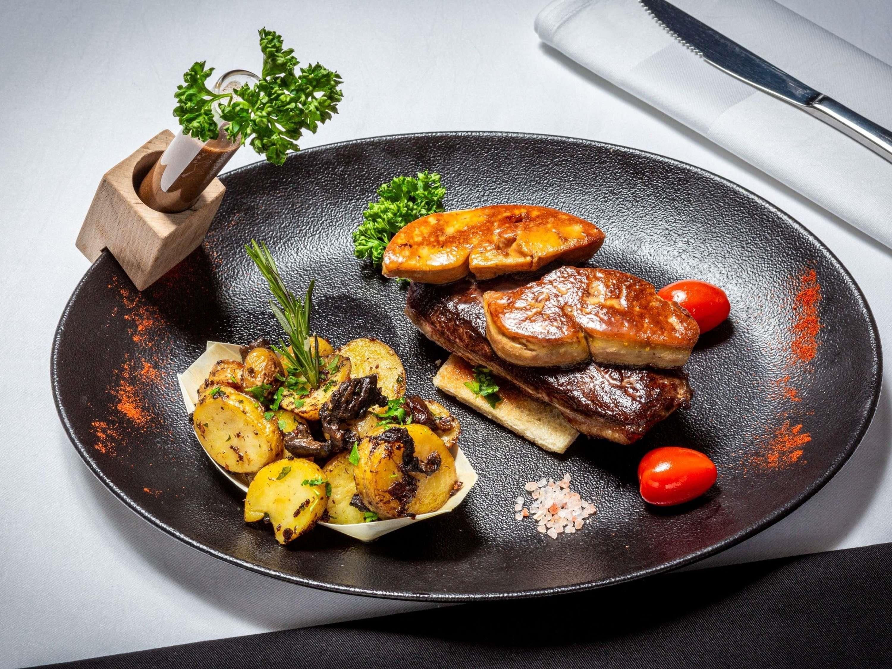 A plate of food with roasted potatoes, meat, and cherry tomatoes.